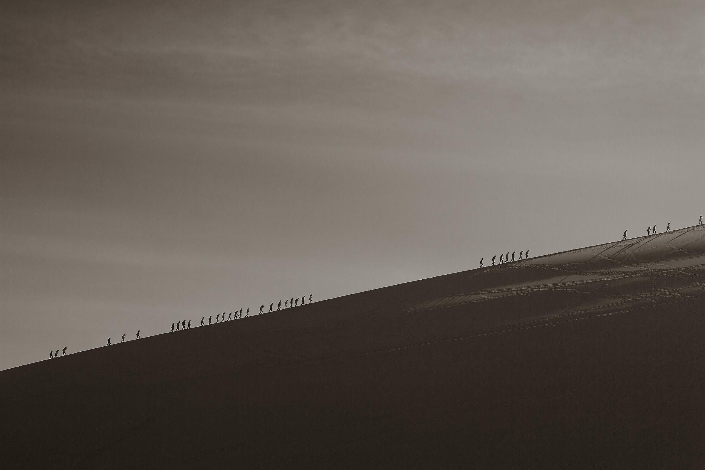 The ascent of men, women and children up large sand dune called Singing Sand Mountain in Dunhuang.